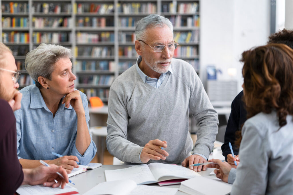 Groupe de personnes âgées assises ensemble, lisant et discutant autour de livres.