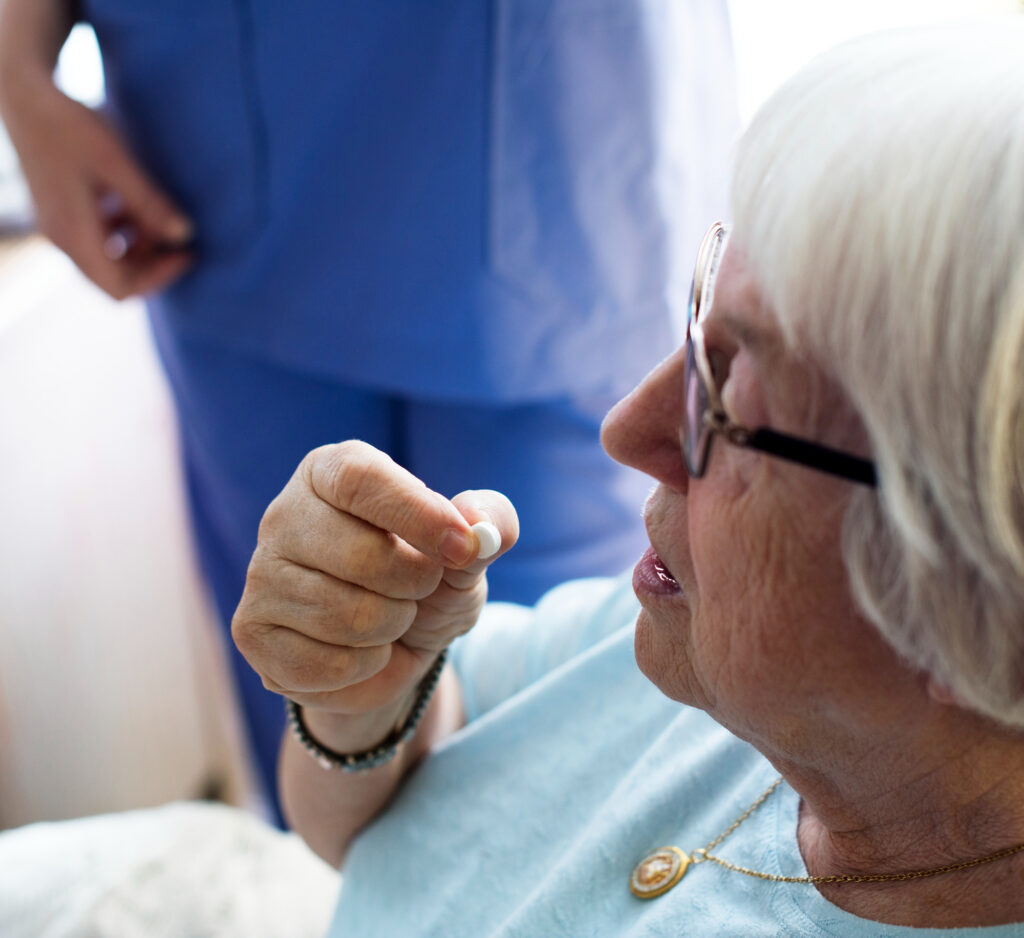 Une femme âgée assise qui prend un médicament assistée d'un membre du personnel médical.
