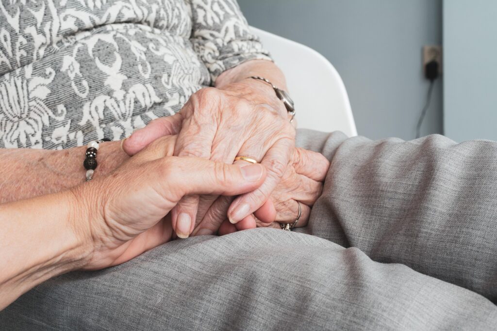 Une personne âgée assise qui se fait tenir la main par un adulte.