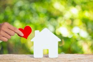 Une main tenant un cœur en papier rouge et une petite maison en bois, symbole de valeurs humaines et de solidarité
