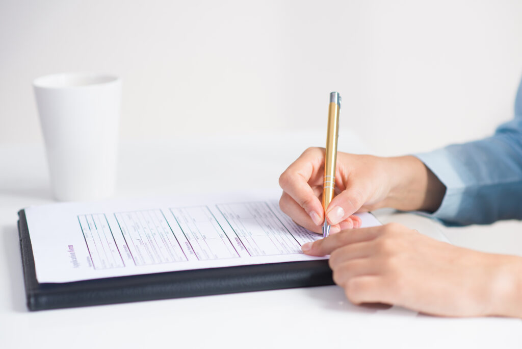 Une personne est en train de signer un formulaire posé sur une planchette sur une table.