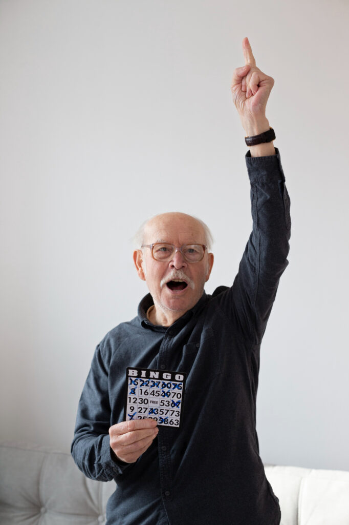 Homme senior souriant levant la main pour annoncer qu’il a gagné au bingo.